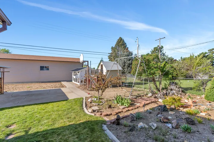 Expansive backyard featuring a manicured lawn, established garden beds with brick edging, a chain-link fence, and a concrete driveway leading to a detached structure