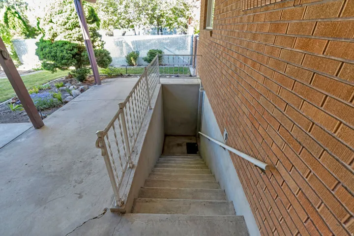 Concrete exterior staircase with a white metal handrail and brick-finish siding