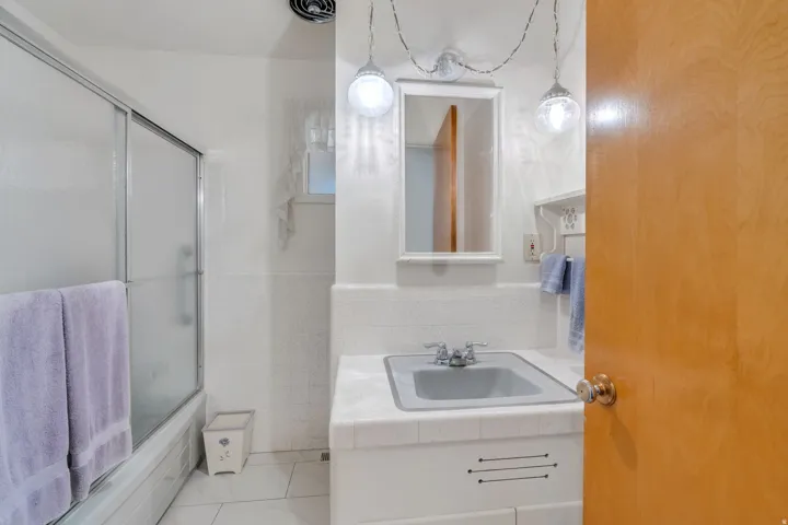 Bathroom featuring a white tile floor, white tiled wainscoting, and a bathtub with a sliding glass enclosure