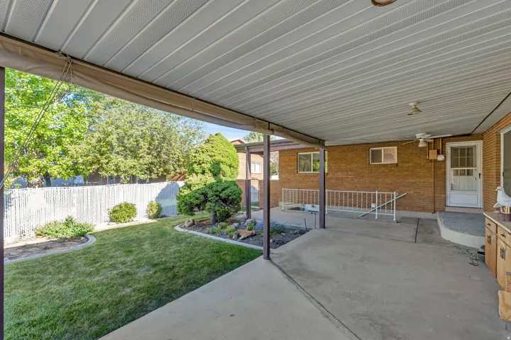 Covered patio area with concrete flooring, brick exterior, and a manicured lawn
