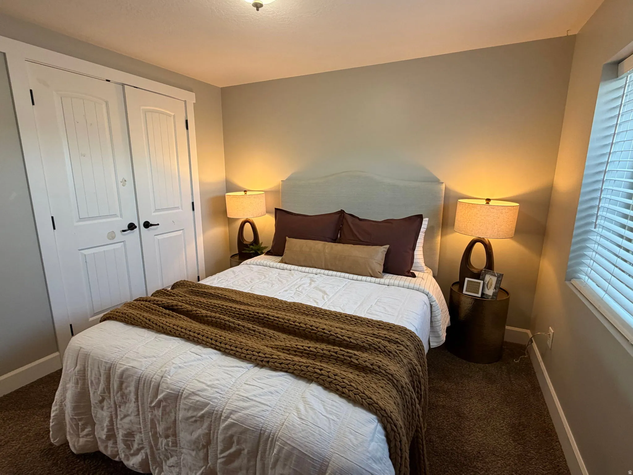 Bedroom featuring light neutral walls, textured brown carpeting, and white window blinds