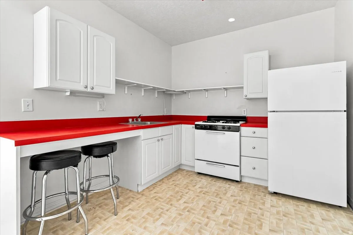 Kitchen featuring white cabinetry, red countertops, a gas range, and a refrigerator