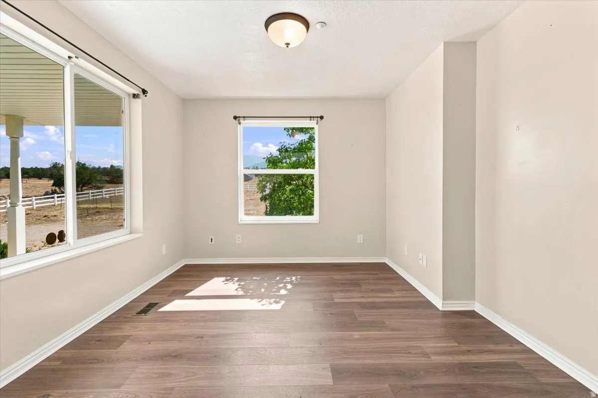 Spacious room featuring wood-finish flooring, two large windows, neutral wall paint, and a semi-flush mount ceiling light