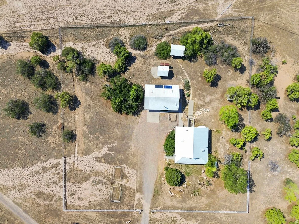 Property perimeter fencing, multiple structures, solar panel installation, mature trees, and an unpaved driveway
