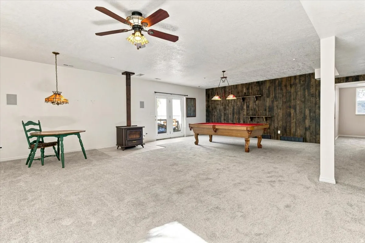 Spacious carpeted room featuring a wood-burning stove, wood accent wall, and built-in ceiling fan with lighting