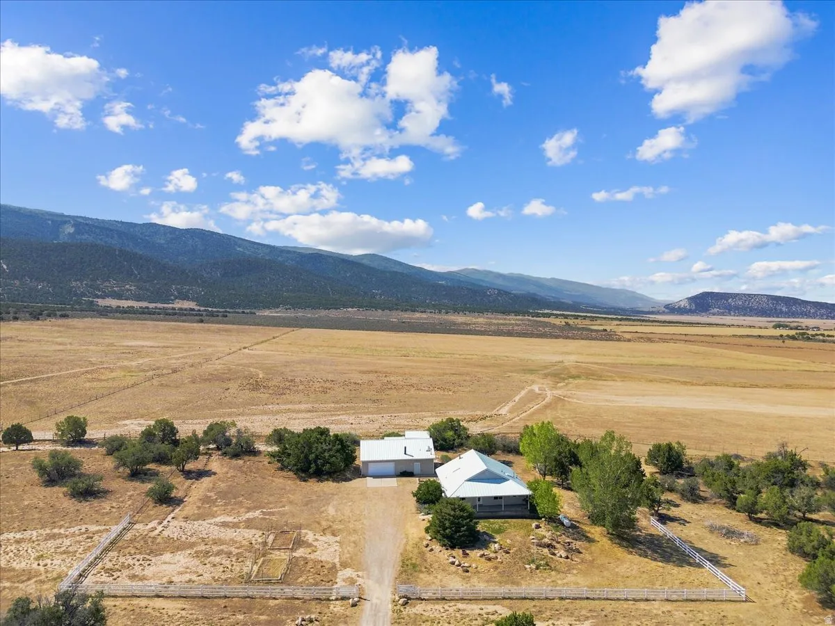 Expansive property featuring a single-story residence, separate outbuilding, surrounding mature trees, and a mountain backdrop