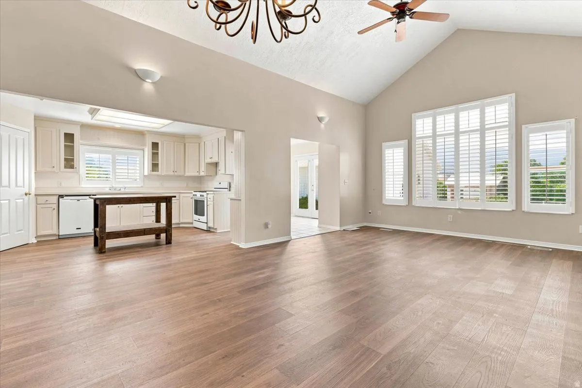 Vaulted ceiling, wood-finish flooring, white plantation shutters, white kitchen cabinetry, and white appliances
