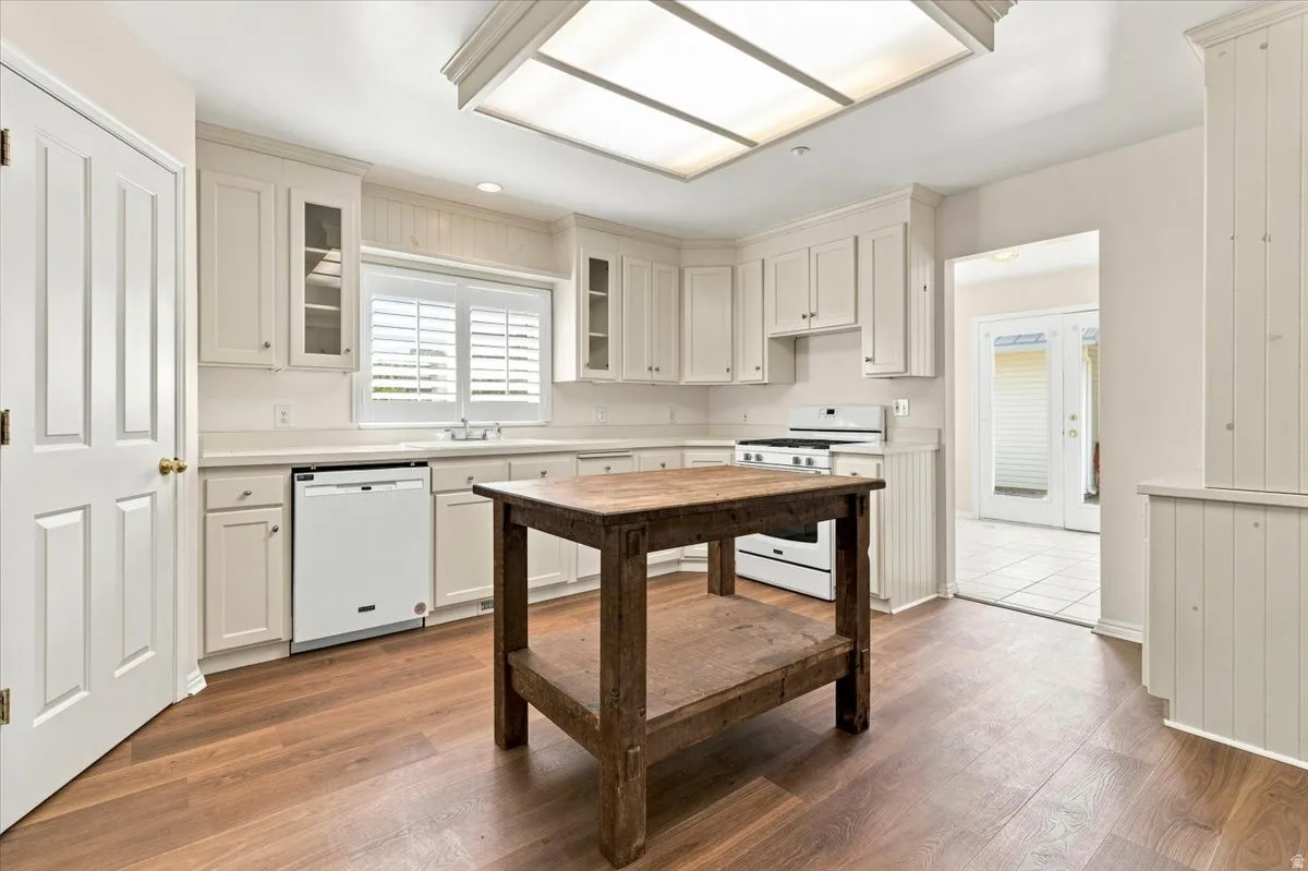 Kitchen featuring white cabinetry, wood-finish flooring, a white gas range, and a built-in dishwasher