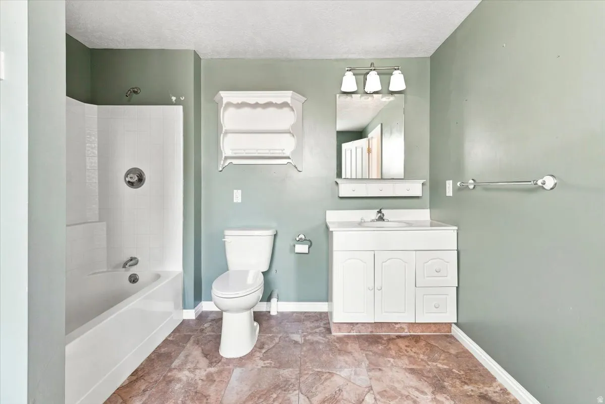 Bathroom featuring a white vanity with integrated sink, a built-in bathtub with shower, and durable tile flooring