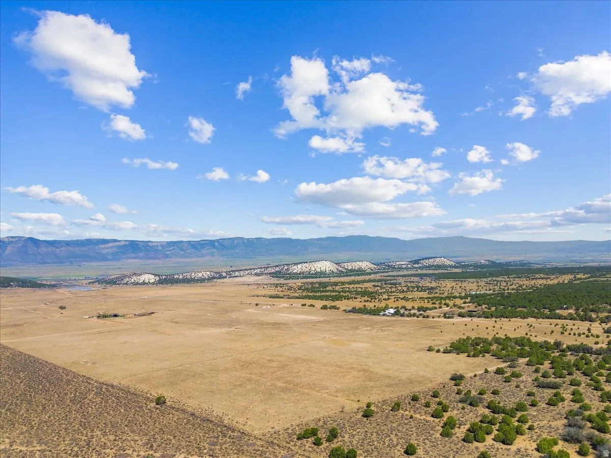 Expansive open landscape with distant mountain ranges, scattered trees, and a clear blue sky with clouds