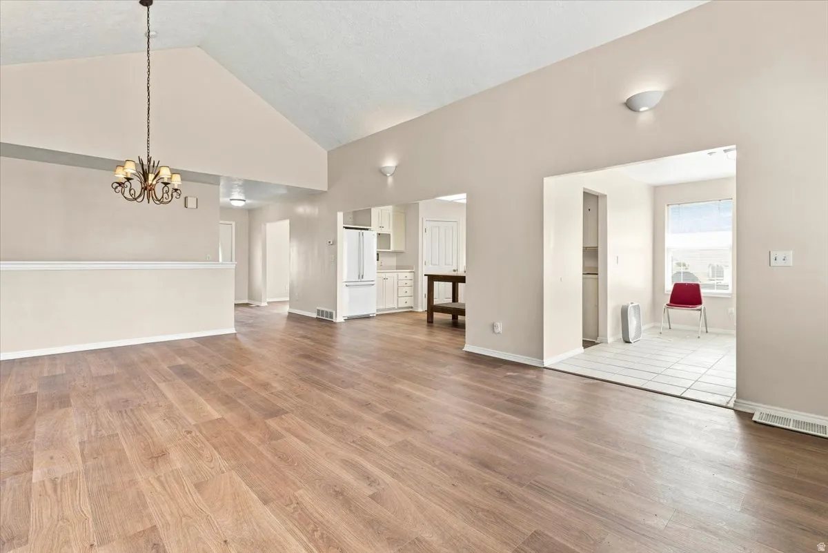 Vaulted ceiling, wood-finish flooring, chandelier, wall sconces, and neutral paint palette