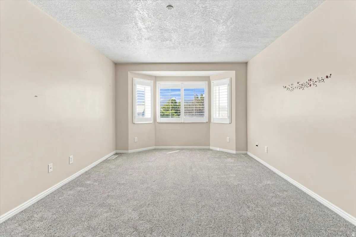 Bay window with plantation shutters, light gray wall-to-wall carpeting, and neutral painted walls