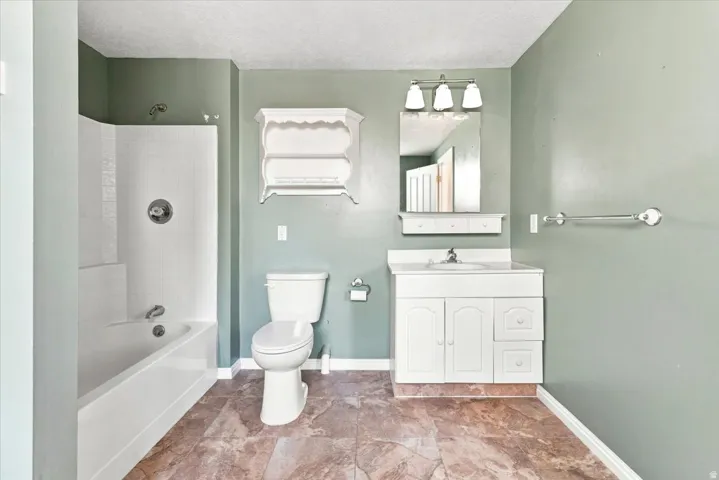 Bathroom featuring a white vanity with integrated sink, a built-in bathtub with shower, and durable tile flooring
