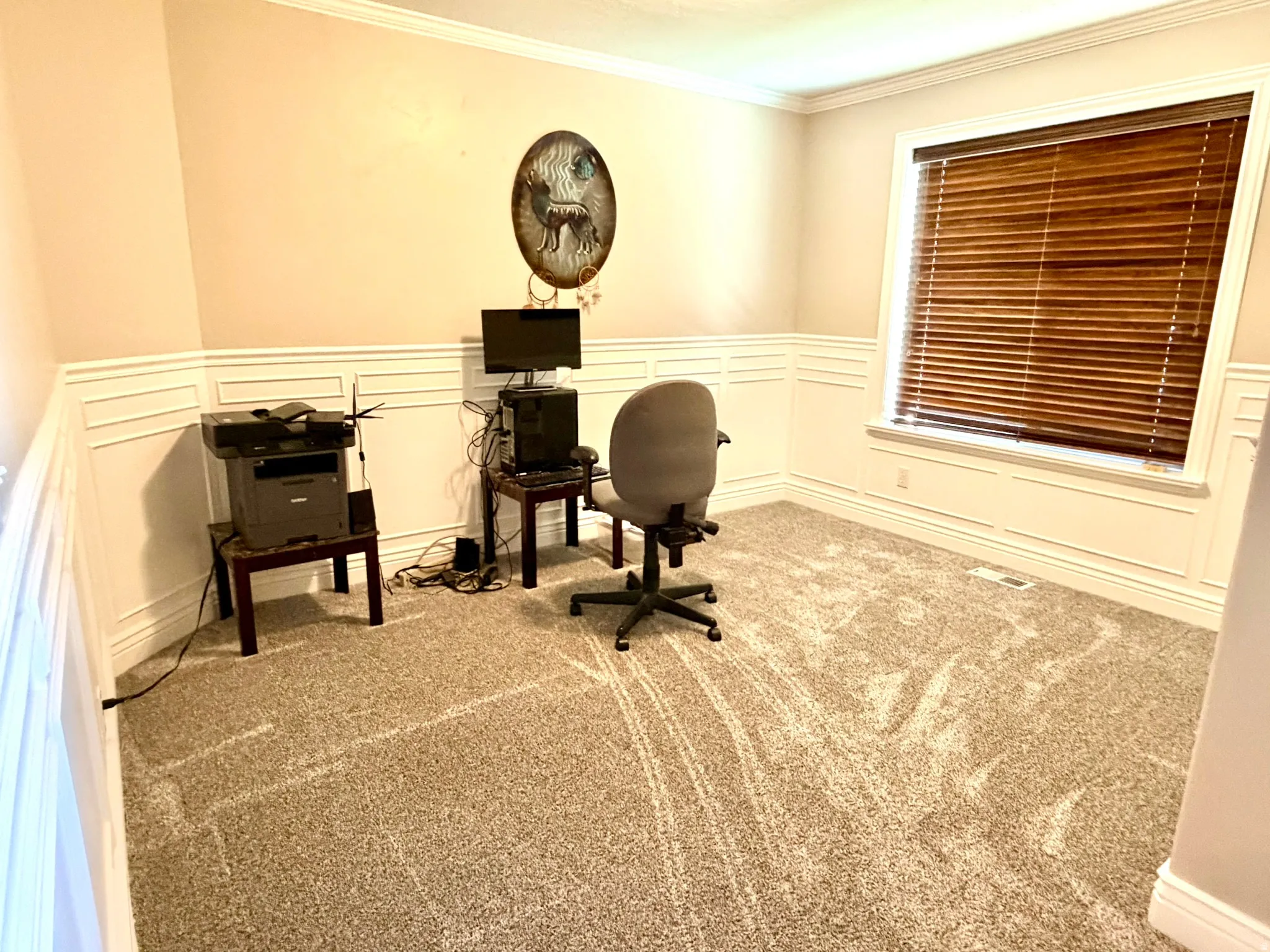 Spacious room featuring patterned carpeting, wainscoting details, a window with wood-finish blinds, and crown molding