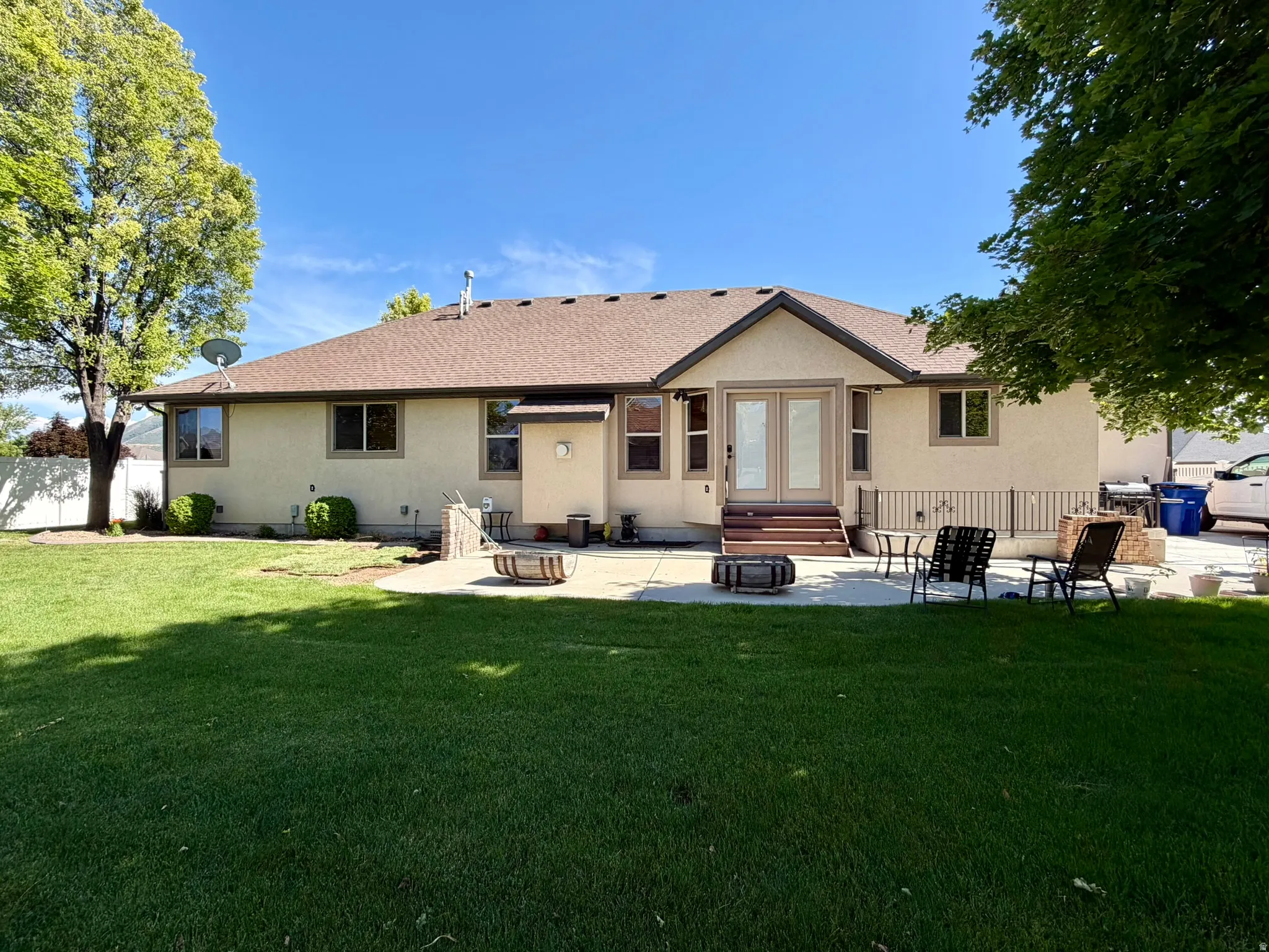 Spacious backyard featuring a large green lawn, mature trees, and a concrete patio with steps leading to a walk-out entrance