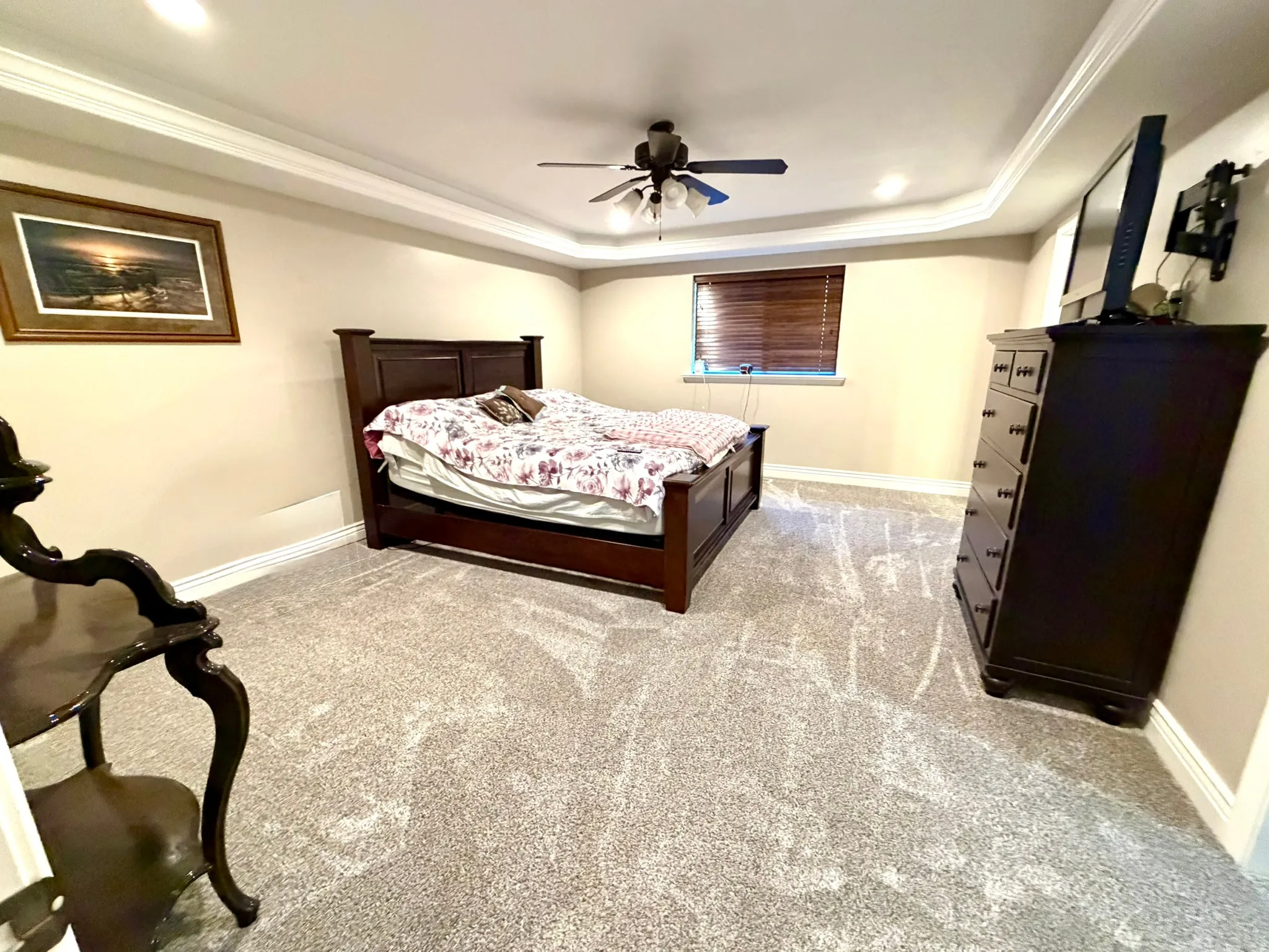 Spacious Primary bedroom featuring plush gray carpeting, crown molding, a ceiling fan with integrated lighting, recessed lighting, and a window with wood-finish blinds