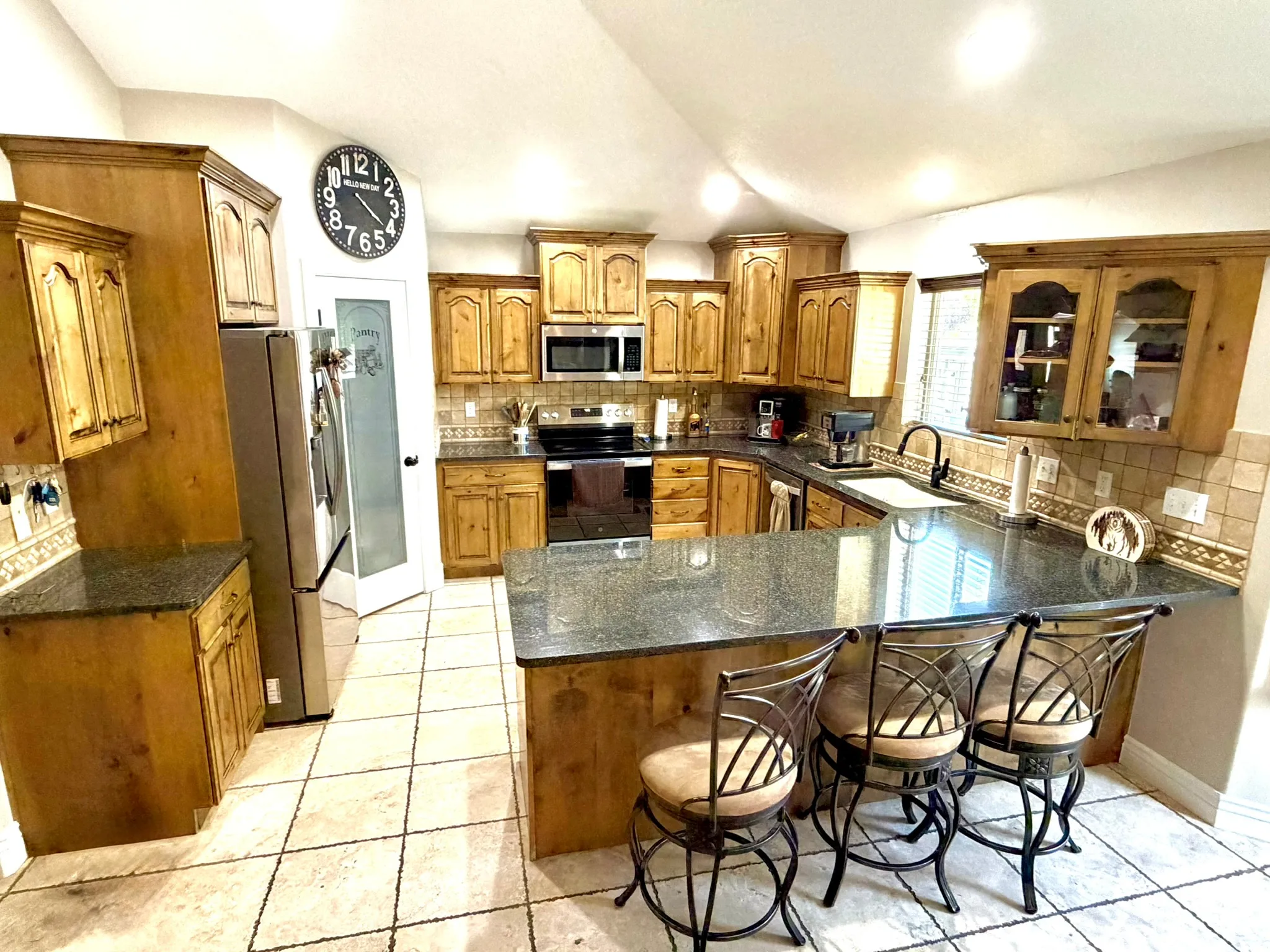 Spacious kitchen featuring wood cabinetry, granite countertops, tile flooring, stainless steel appliances, and a built-in kitchen island with seating