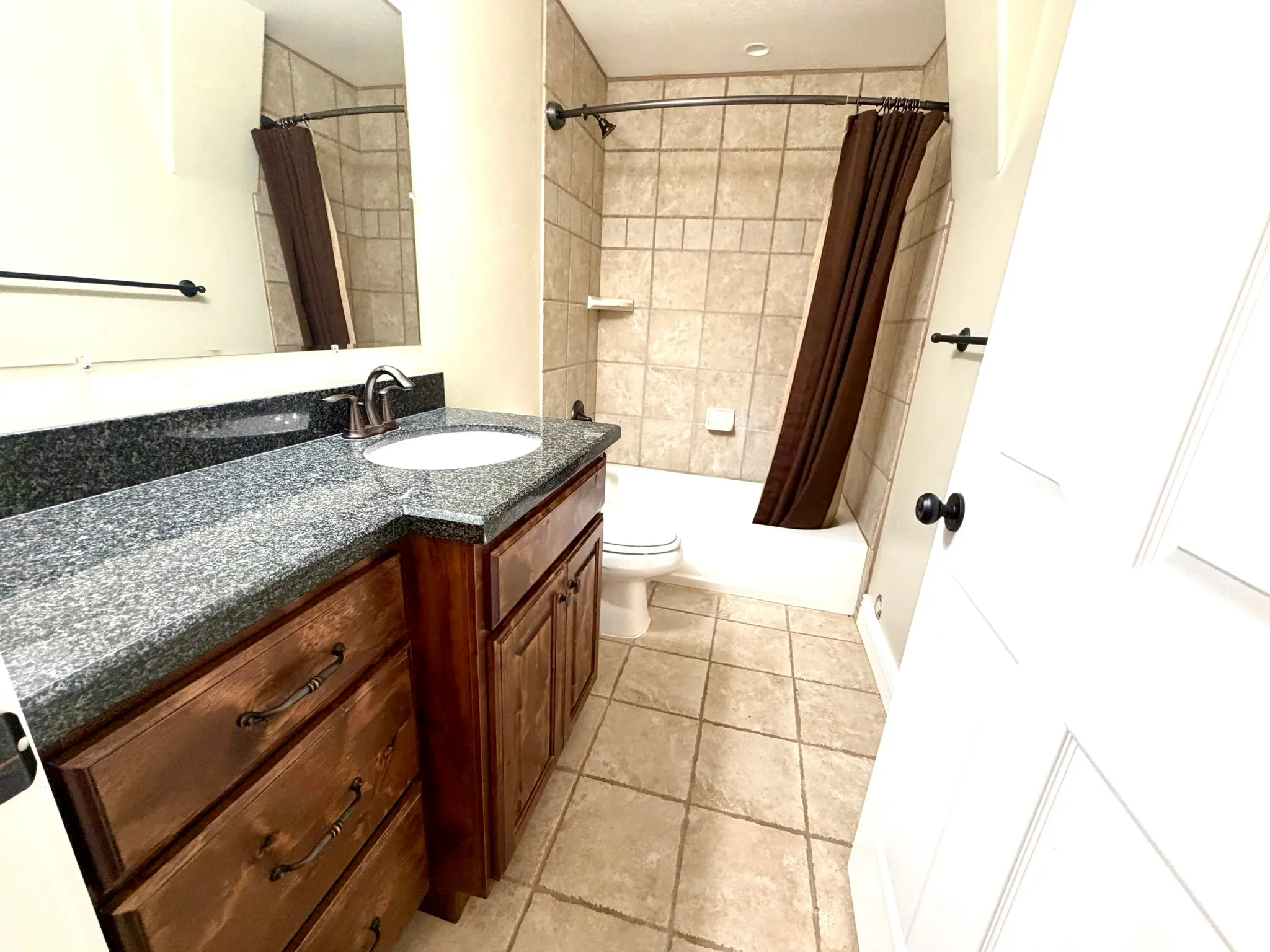 Full Bathroom featuring a dark granite countertop with an undermount sink, rich wood-finish cabinetry, a tiled shower/tub combination, and tiled flooring
