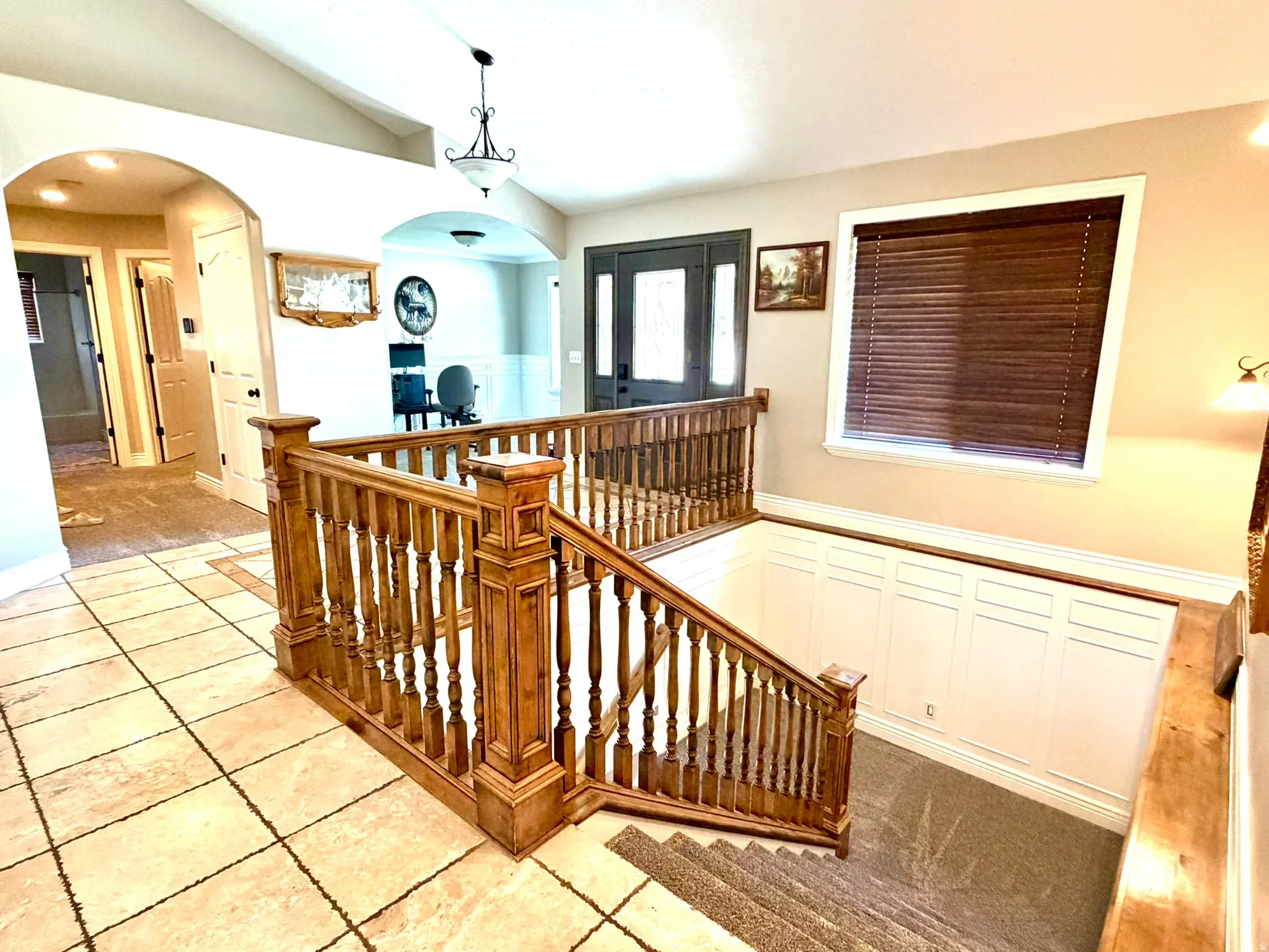 Grand entryway featuring a wood baluster staircase, tile flooring, arched doorways, vaulted ceilings, and wainscoting