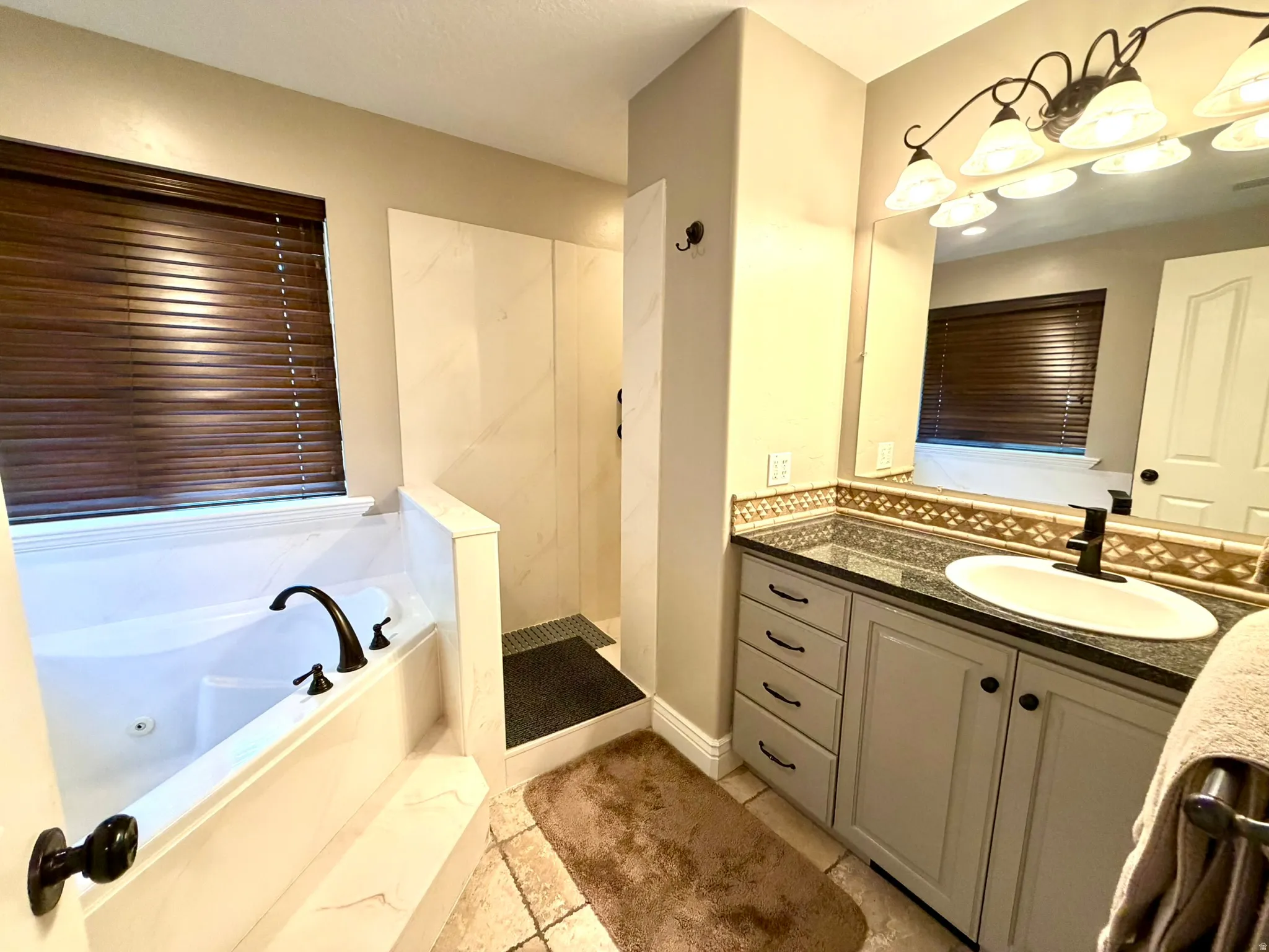 Primary bathroom featuring a built-in jetted tub with dark bronze fixtures, a walk-in shower with tile surround, and a single vanity with a granite-finish countertop