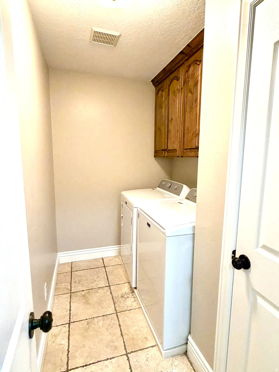Laundry area featuring tiled flooring, crown molding, wood-finish cabinetry, and a ceiling ventilation system