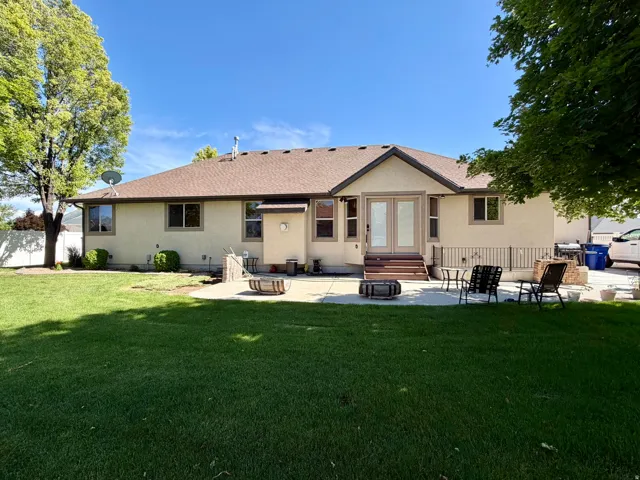 Spacious backyard featuring a large green lawn, mature trees, and a concrete patio with steps leading to a walk-out entrance