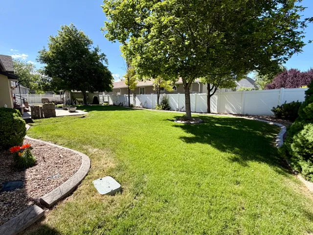Expansive backyard featuring a lush lawn, mature trees, concrete patio, white privacy fencing, and decorative rock landscaping with concrete curbing