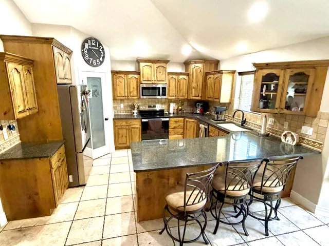 Spacious kitchen featuring wood cabinetry, granite countertops, tile flooring, stainless steel appliances, and a built-in kitchen island with seating