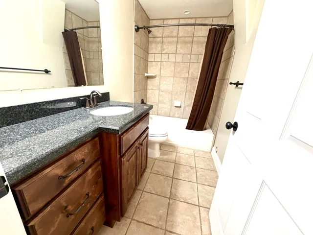 Full Bathroom featuring a dark granite countertop with an undermount sink, rich wood-finish cabinetry, a tiled shower/tub combination, and tiled flooring