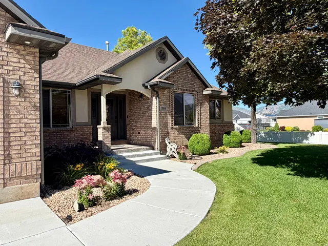 Brick and stucco exterior with a covered entry, concrete walkway, and established landscaping