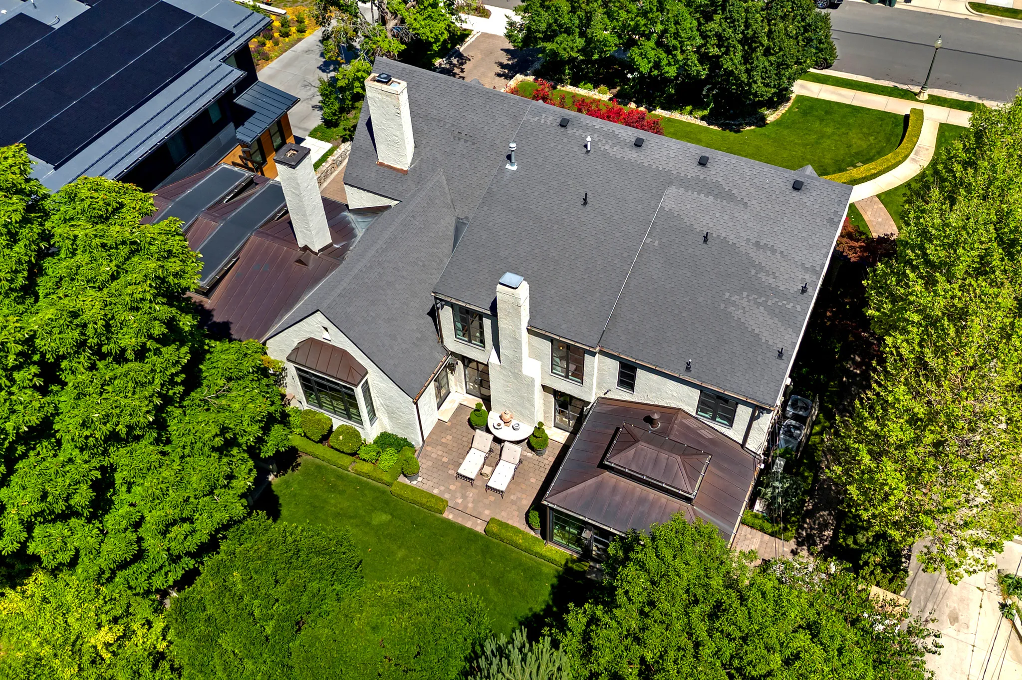 Expansive rear facade featuring a paver patio, multiple chimneys, and mature perimeter landscaping