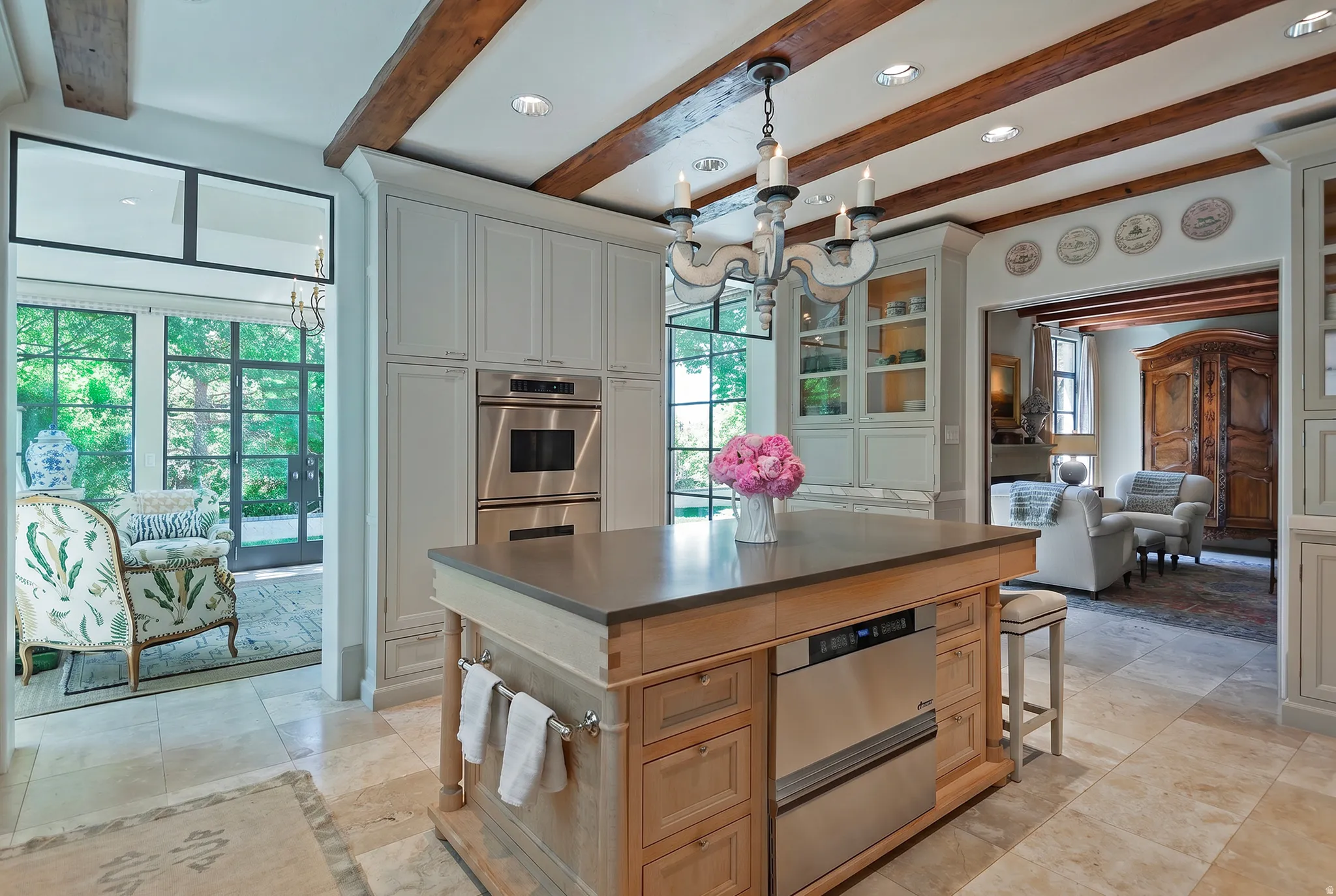 Gourmet kitchen featuring a substantial wood island with stone countertop, integrated stainless steel appliances, extensive custom cabinetry, and exposed ceiling beams