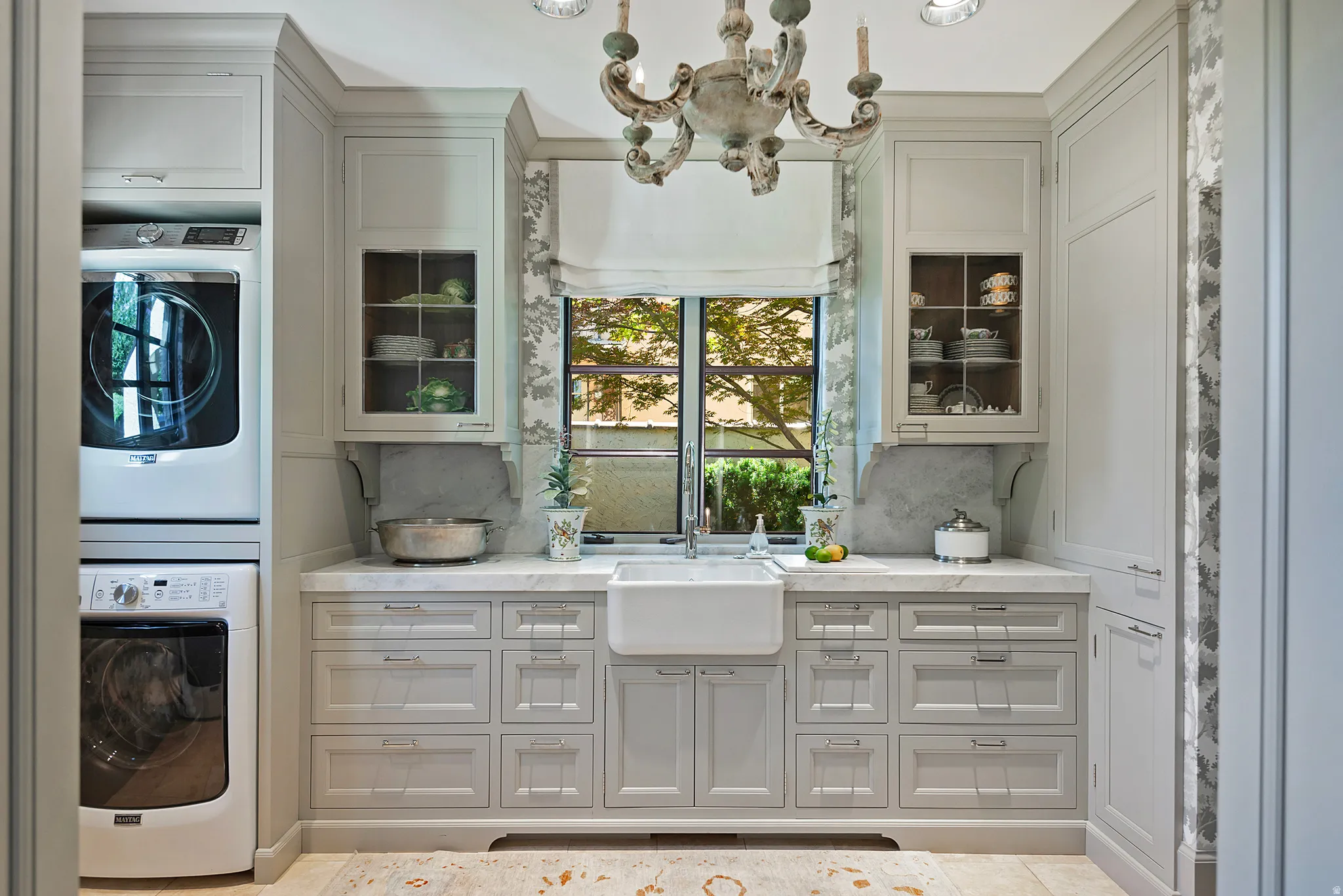 Utility room featuring a farmhouse sink, marble-finish countertops, extensive light-colored cabinetry, integrated laundry appliances, and a decorative chandelier