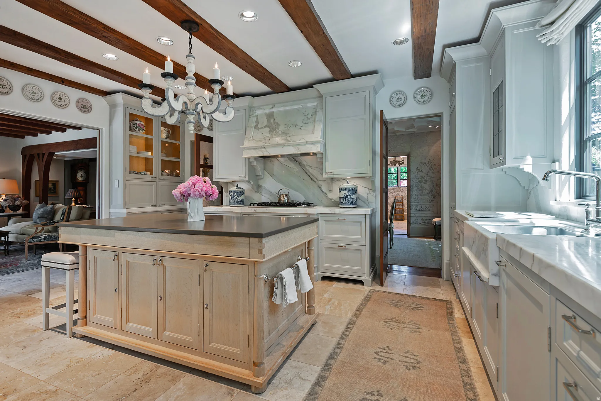 Gourmet kitchen featuring a substantial island, wood-finish ceiling beams, travertine flooring, and custom cabinetry