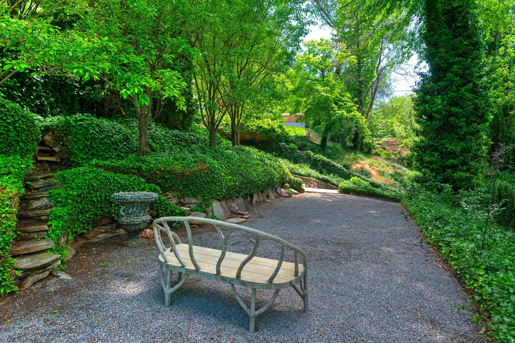 Gravel pathway bordered by lush greenery and mature trees