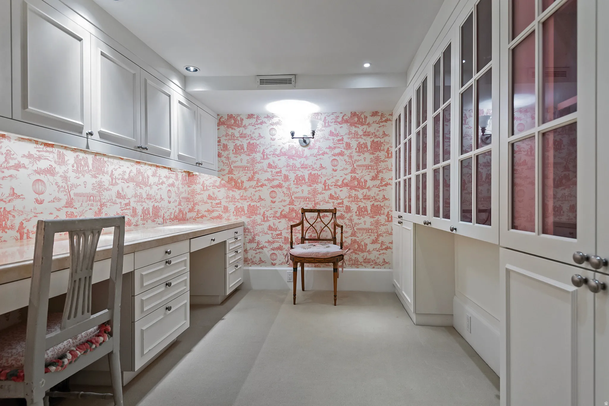 Dedicated workspace featuring extensive built-in cabinetry, dual desk areas with stone-finish countertops, and decorative patterned wallpaper