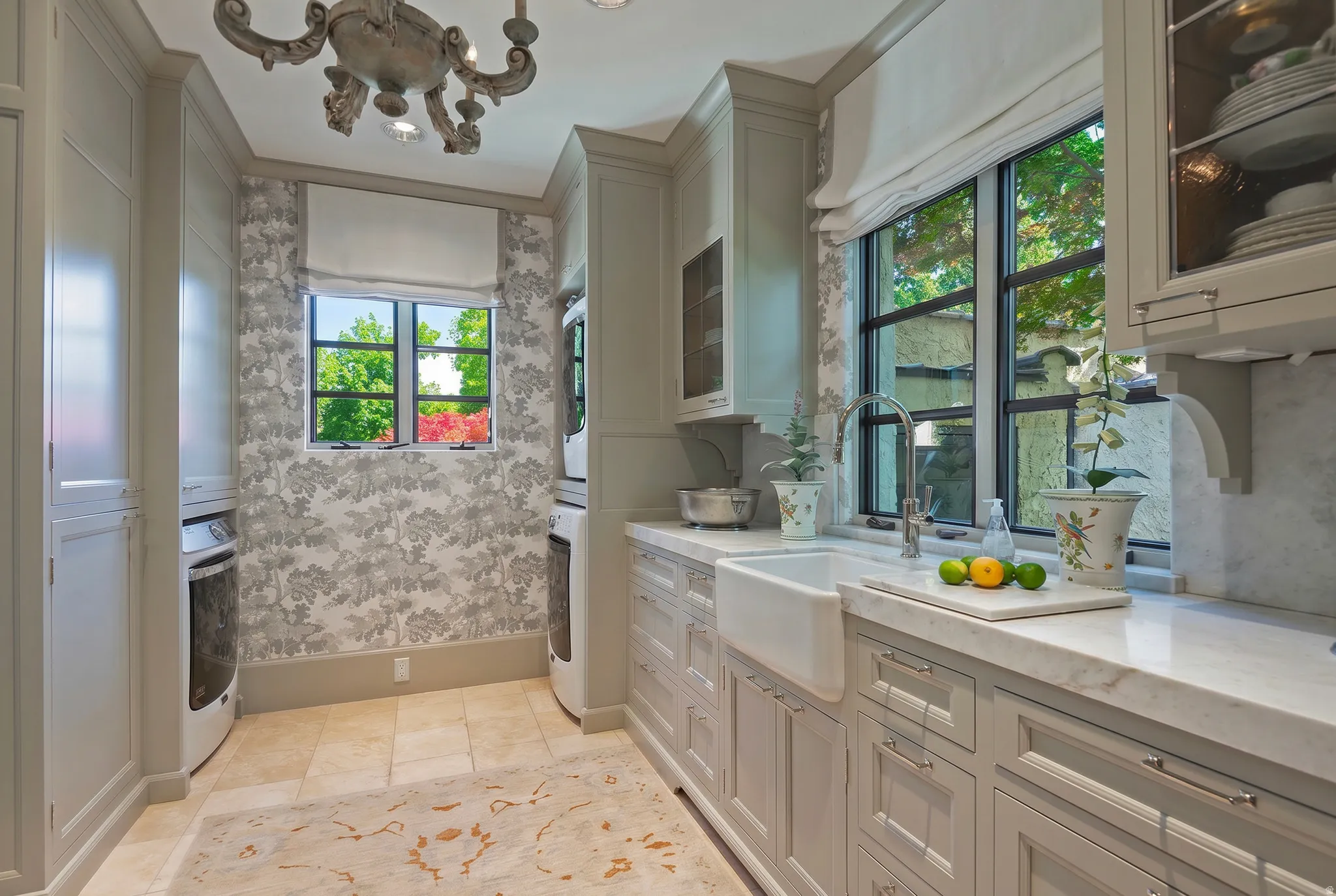 Utility room featuring a farmhouse sink, stone countertops, custom cabinetry with glass-front uppers, patterned wallpaper, and transom windows
