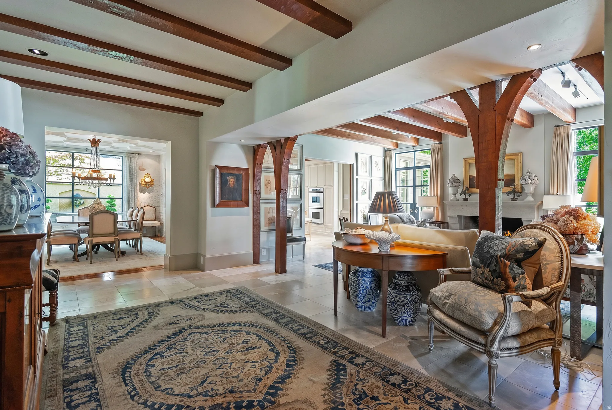 Open-concept living space featuring wood ceiling beams, light-toned tile flooring, and arched wood columns