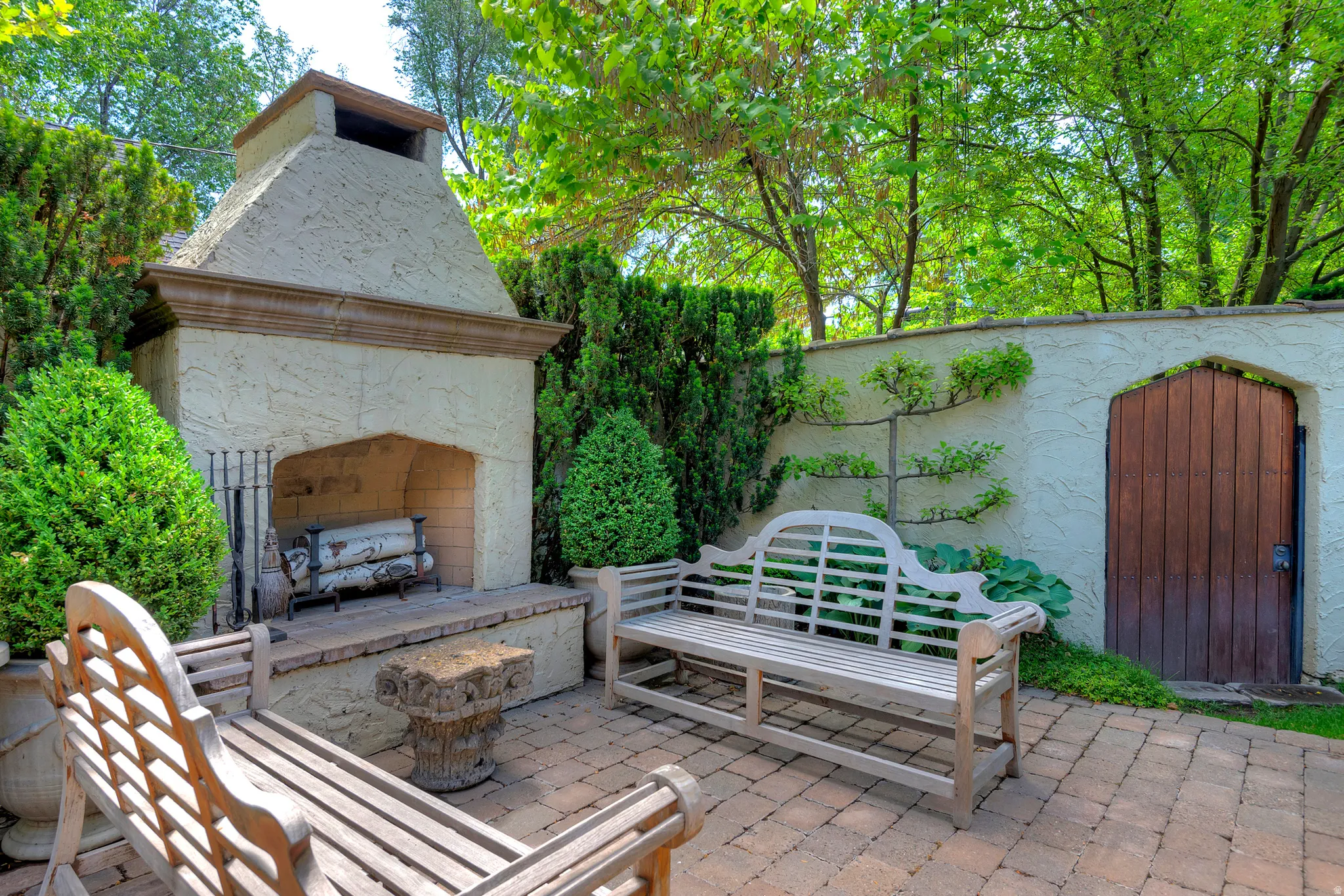Outdoor living area featuring a stucco fireplace with a stone mantel, a privacy wall with a wooden arched door, and paver flooring