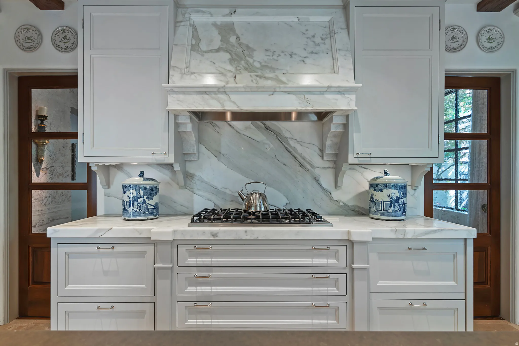 Gourmet kitchen featuring a built-in gas range, full-height veined stone backsplash, custom cabinetry with under-cabinet lighting, a stone range hood, and wood-finish doors
