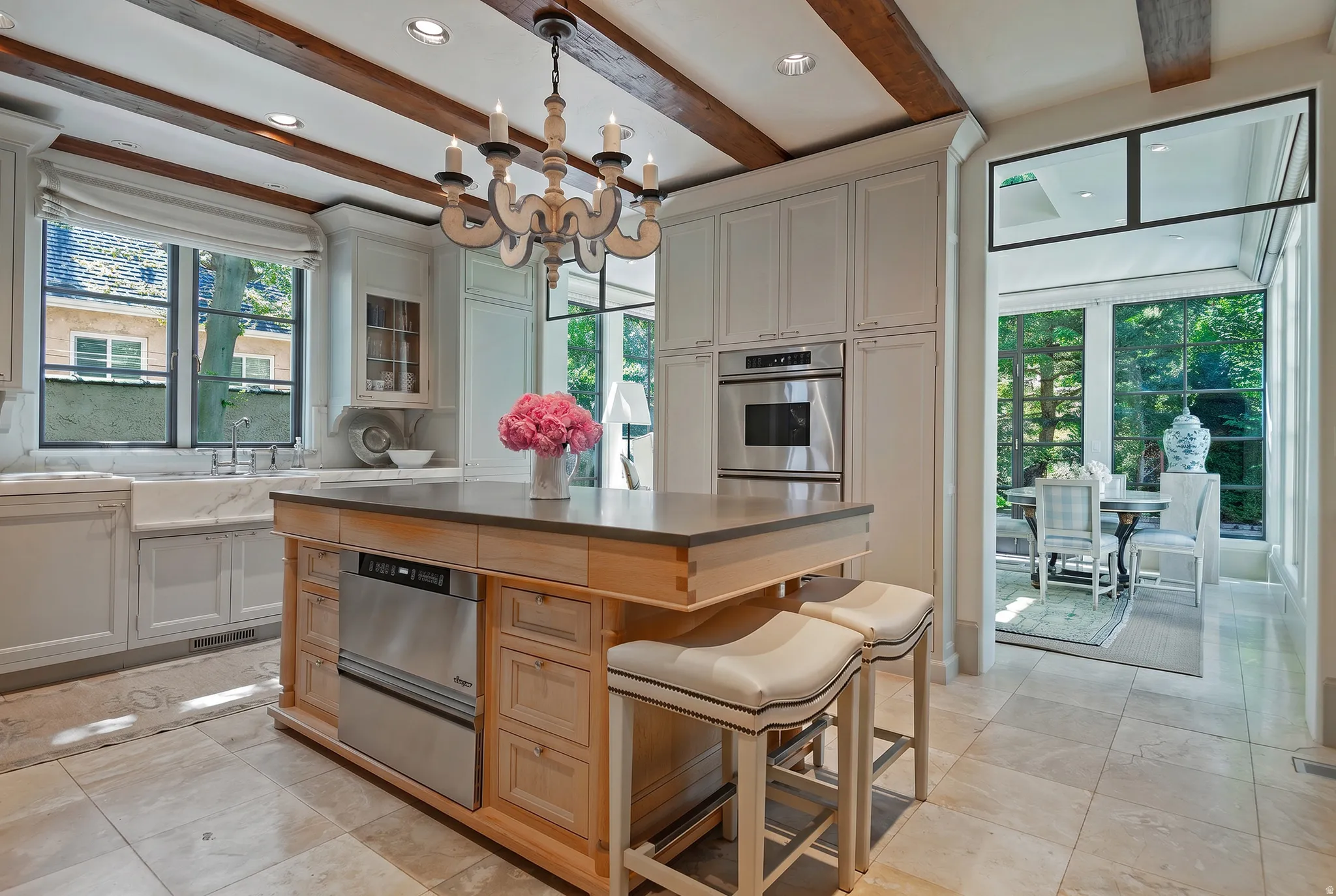 Gourmet kitchen featuring a substantial wood island with stone countertop, stainless steel appliances, exposed wood beam ceiling, and stone tile flooring