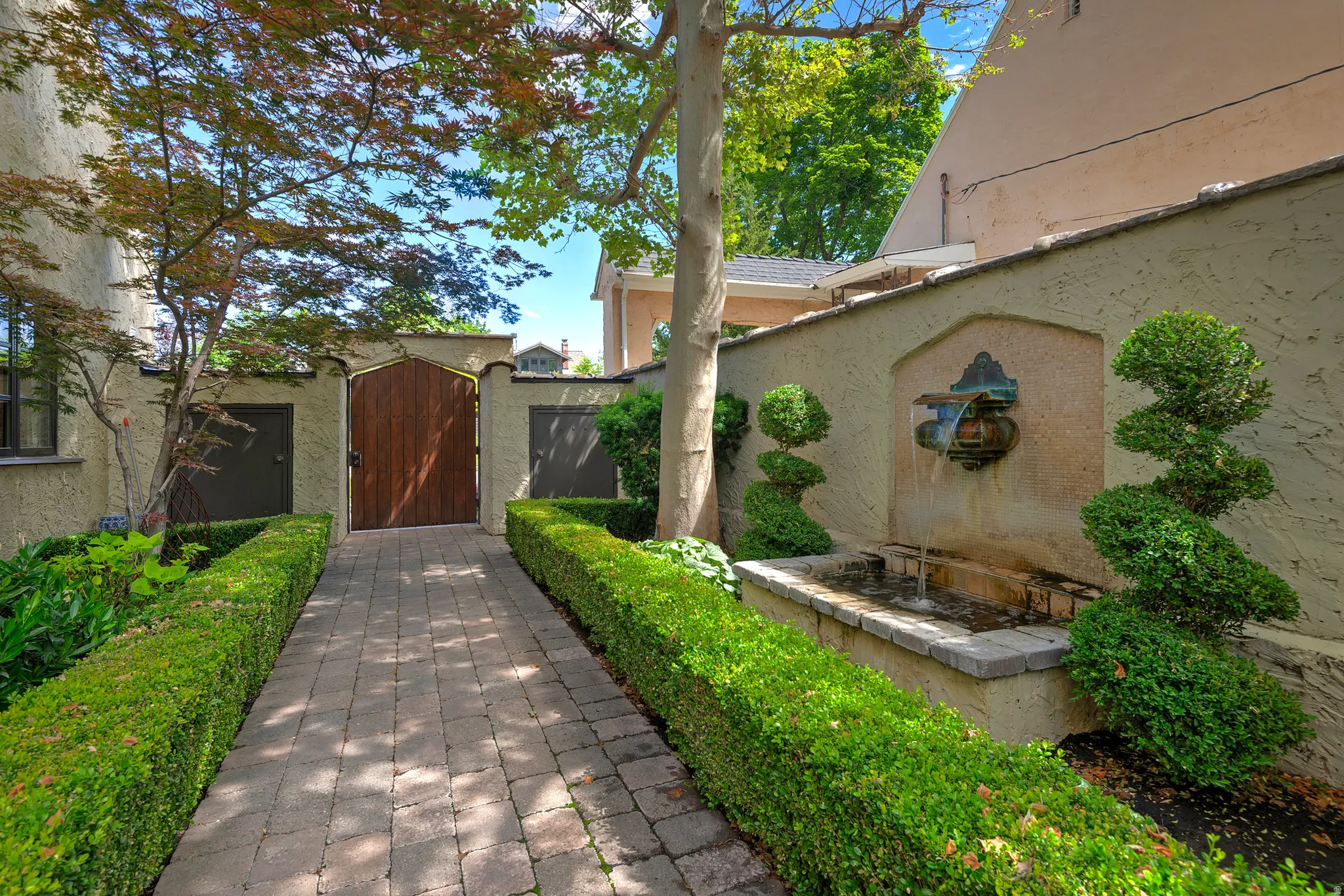 Paver pathway framed by manicured hedge rows, leading to a wooden arched gate