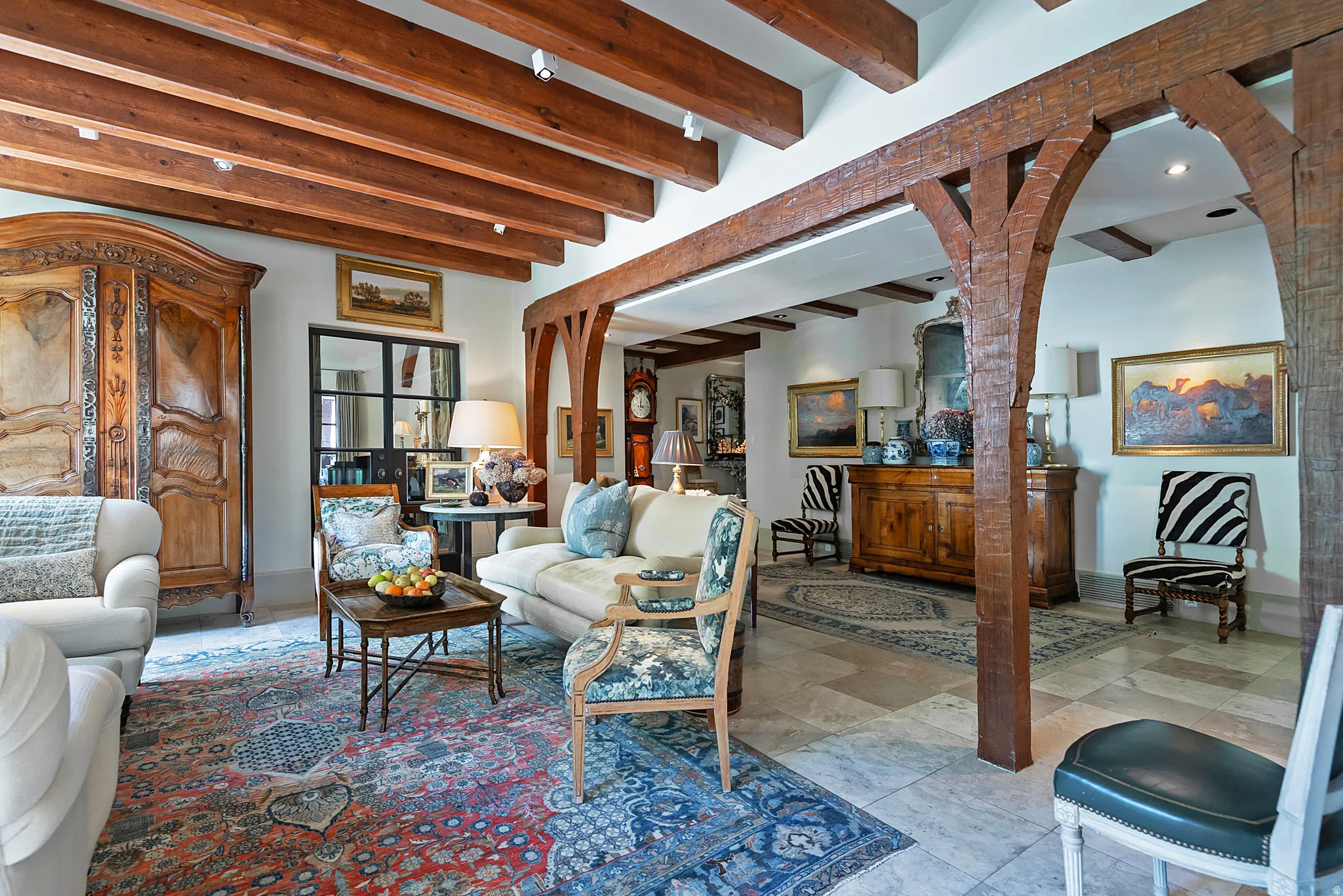 Vaulted ceiling with exposed wood beams, archway with substantial wood pillars, light-toned tile flooring, recessed lighting, and a large black-framed window