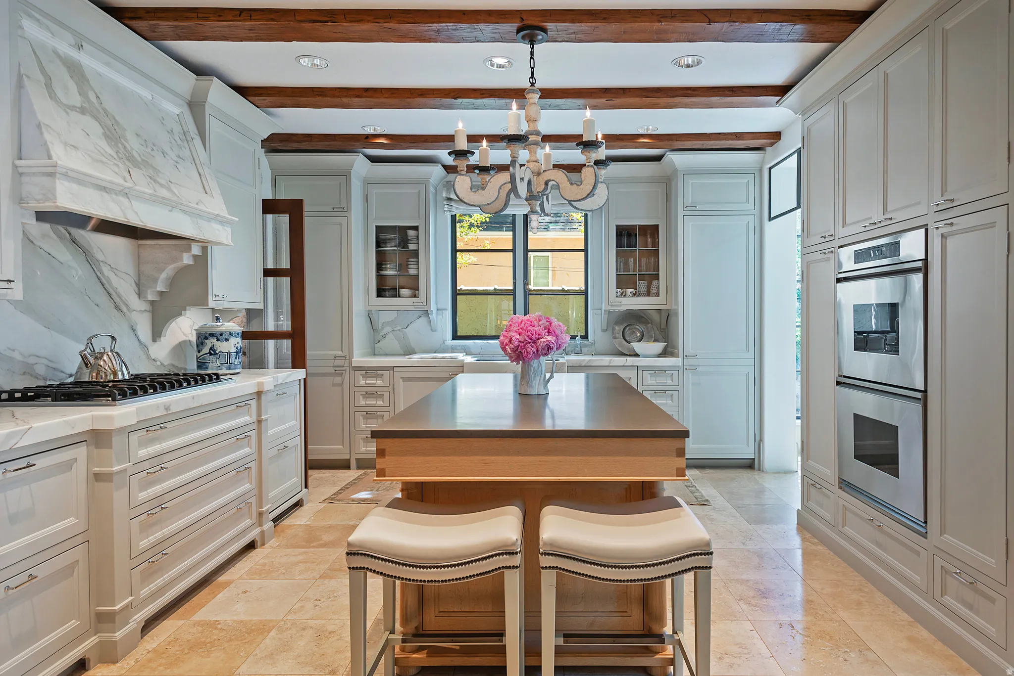Gourmet kitchen featuring a substantial central island, professional-grade stainless steel double ovens, custom cabinetry, a five-burner gas range, and wood beam ceilings