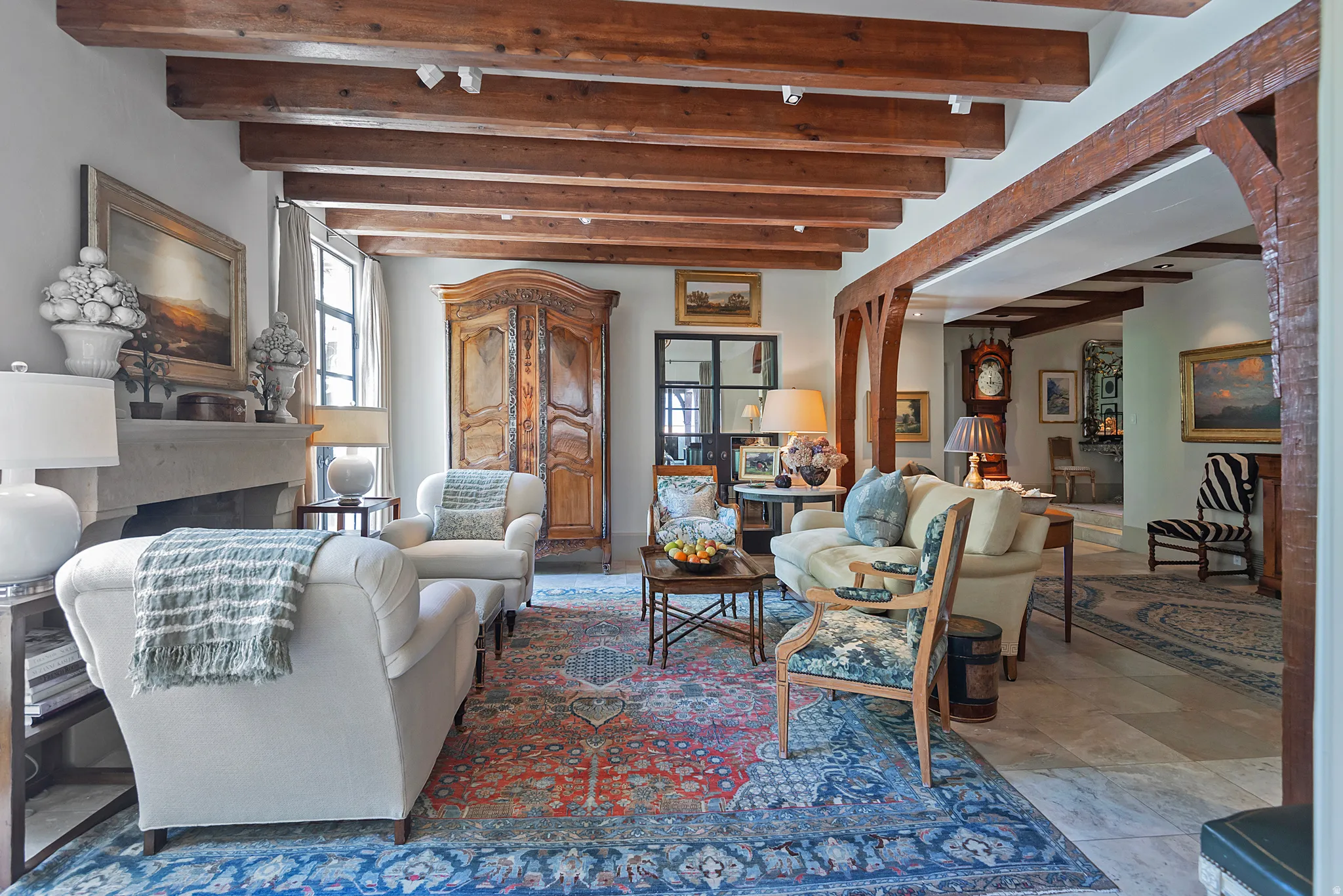 Living area featuring exposed wood beams, light-colored walls, a stone fireplace, and light-toned flooring