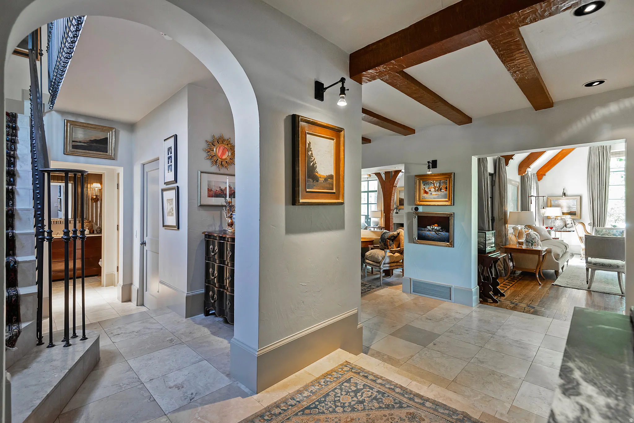 Entryway featuring stone tile flooring, exposed wood ceiling beams, arched architectural details, and a wrought iron staircase