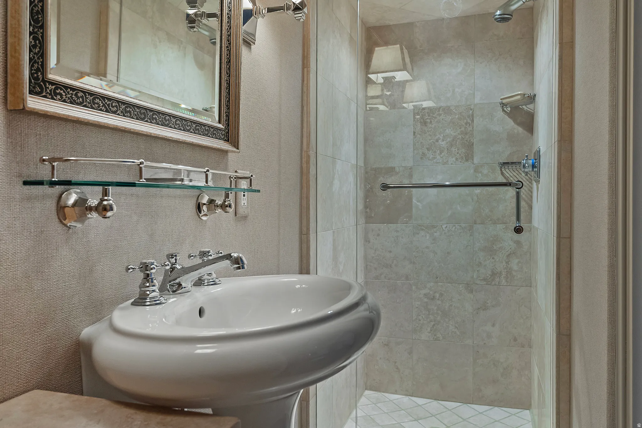 Pedestal sink with polished chrome fixtures, framed mirror, and glass shelf