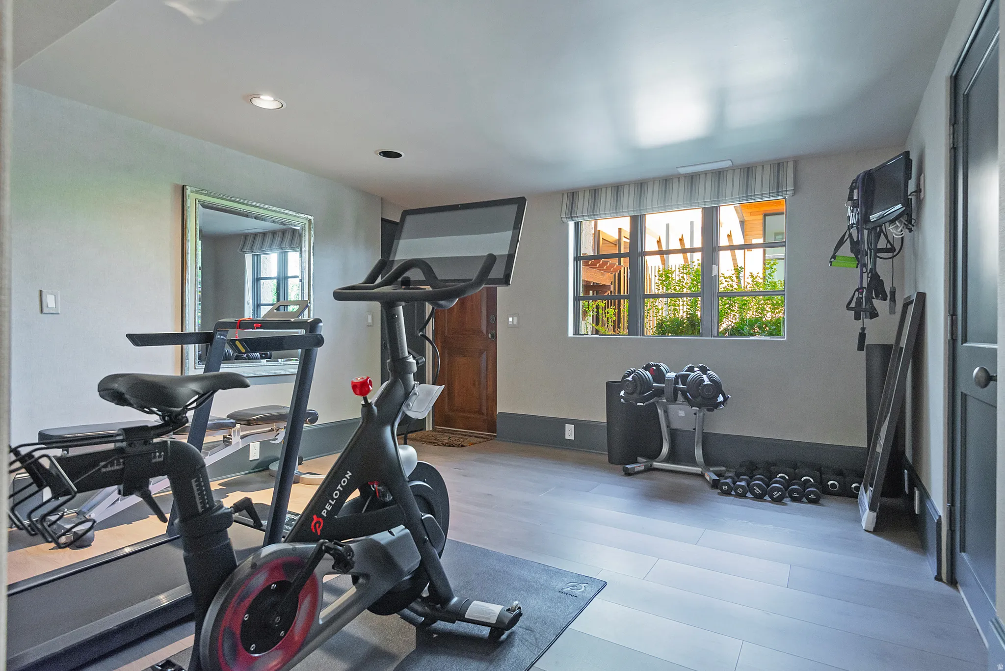 Dedicated fitness space featuring light wood-finish flooring, recessed lighting, and a window with custom window treatments