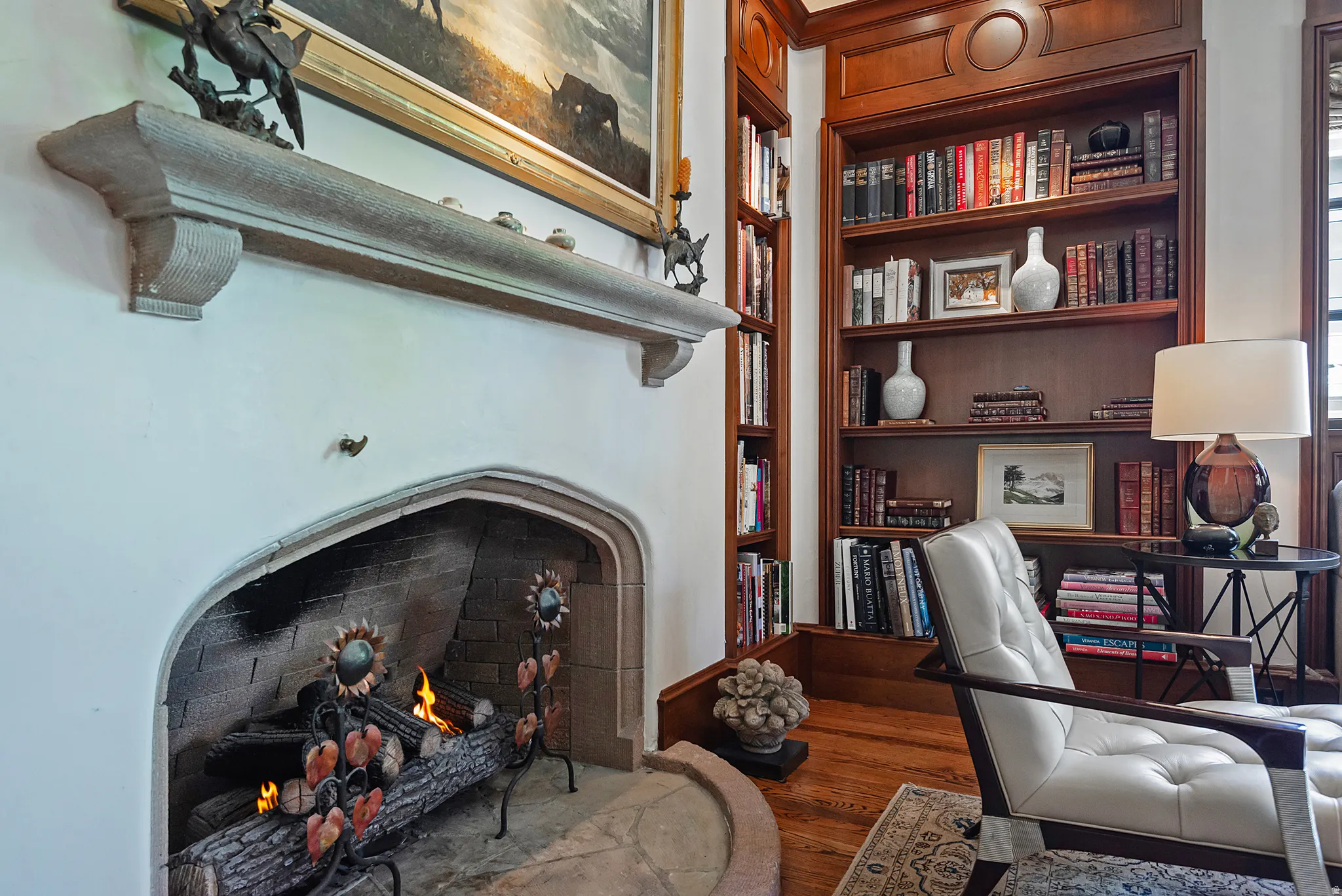 Stone fireplace with an arched opening, detailed mantel, built-in shelving, wood-finish flooring, and crown molding