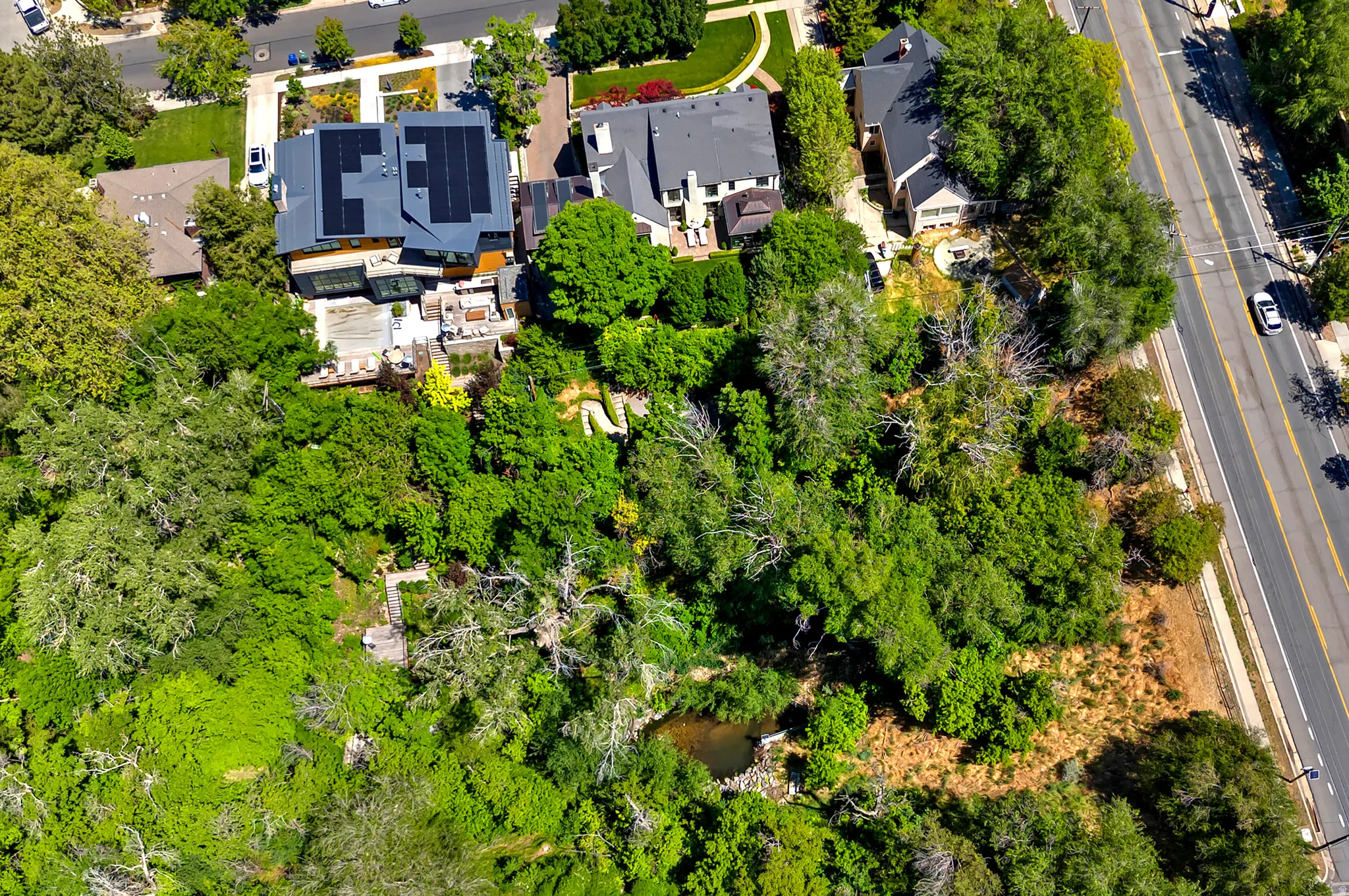 Modern architectural residence featuring a dark-toned roof with solar panels, multiple outdoor patio areas, and a lush, tree-filled landscape